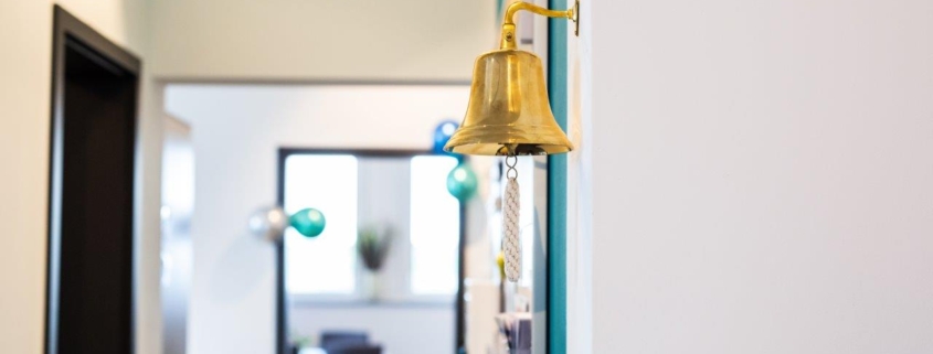 Goldene Glocke an der Wand eines Büroflurs im Lean Service Institute, Symbol für Erfolge und Teamrituale, im Hintergrund ein Besprechungsraum.